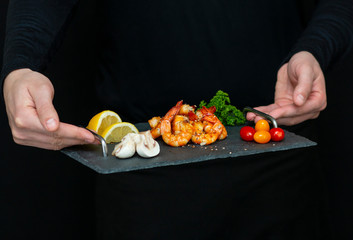man holds fresh, tasty shrimp on a stone black tray