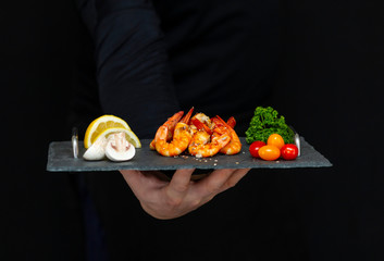 man holds fresh, tasty shrimp on a stone black tray