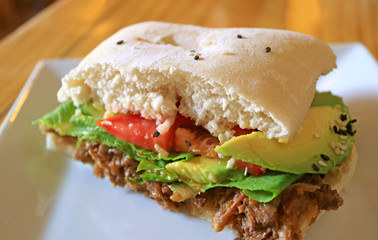 Sliced beef with fresh vegetable sandwich cut in half on a white plate