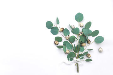 Easter bouqet composition of eucalyptus leaves and quail eggs with lace ribbon on white background. Flat lay, top view. copy space