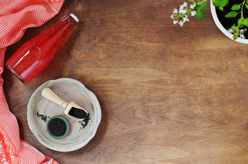 Glass bottle of strawberry juice with Basil seeds. A ceramic plate with a gravy boat and a scoop of Basil seeds, a linen towel and a pot of blooming flowers. Top view, horizontal position, copy space