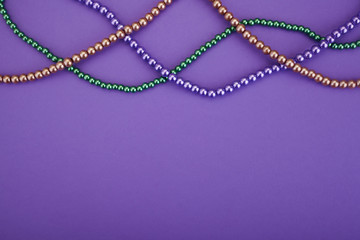 Mardi Gras three colours beads on purple background. Space for text. Top view