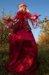 Sensual blond girl in fantasy red fairy tale stylization in apple park.