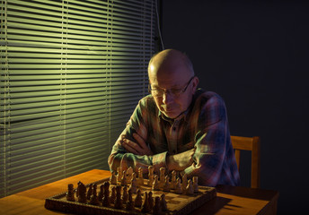 Man playing chess beside windows wtih blinds