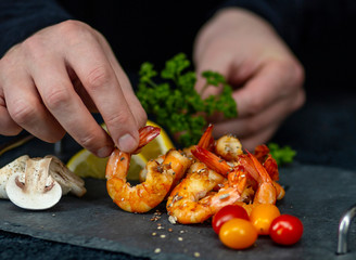 man decorates a dish of fried shrimp with vegetables on a stone tray