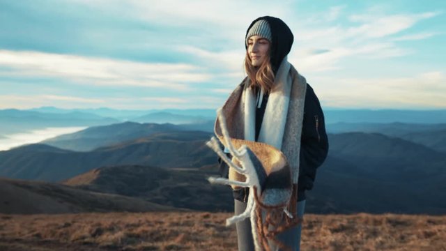 Caucasian beautiful young woman standing on mountain top enjoying amazing view her scarf flutters in the strong wind. Adventur relaxation pure nature hipster fresh air slow motion sun shine