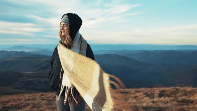 Close up view of pretty stylish young woman staying on mountain top enjoying amazing view, strong view blowing the scarf Adventur relaxation pure nature hipster fresh air slow motion sun shine