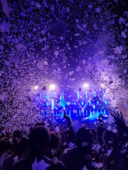 Fototapeta na wymiar Menschen feiern mit Armen in der Luft vor einer Bühne auf einem Musikfestival mit Konfetti und bunten Scheinwerfern