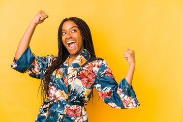 Young african american woman wearing an asiatic pijama isolated raising fist after a victory,...