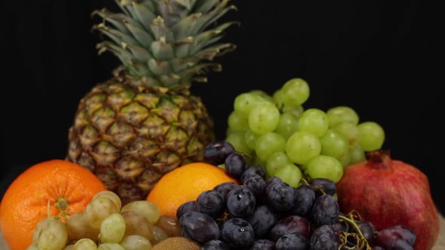 A lot of fruits lie on a silver tray on a black background, close-up