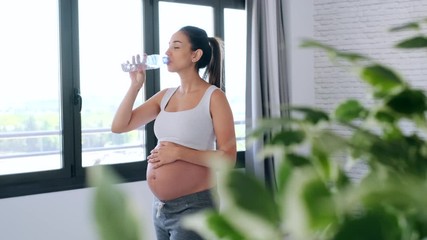 Video of pretty young pregnant woman drinking water while standing at home.