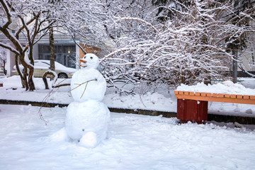 A smiling snowman with a pinecone nose near a bench