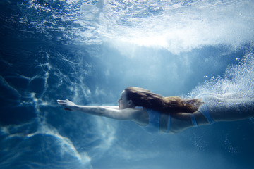 Woman dives under water among the rays of light and air bubbles