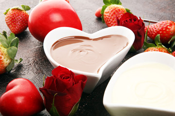 Valentine Chocolate fondue melted with fresh strawberries and dark and white chocolate. Red roses and sugar hearts for Valentines Day. Valentine Background