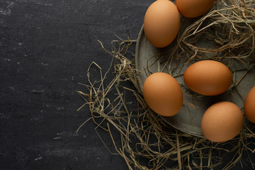 Chicken eggs on green plate and hay with gray background, flat lay