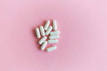 A pile of medicinal white capsules on a pink background. Free space for text