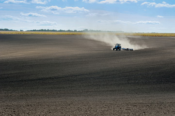 blue tractor on the plowed field performs the preparation for sowing.