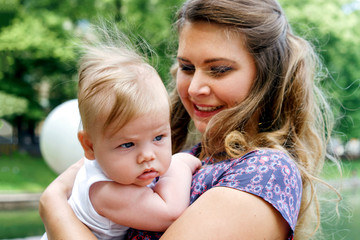 Pretty blond long heared mom and newborn son in her arms in the summer park. The concept summer walking with small children outdoors 