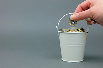 A hand adding a pound coin to a bucket full of cash.