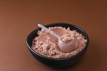 Scoop of chocolate whey protein in a black bowl. The concept of healthy eating and vitamins.