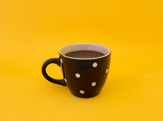 Lonely black cup of espresso with white dots on isolated yellow background