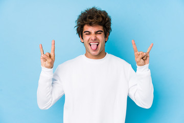 Young caucasian man against a blue background isolated showing rock gesture with fingers