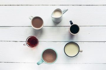 Five different hot drinks and jug of non dairy vegan milk on white wooden table. Hot chocolate,...