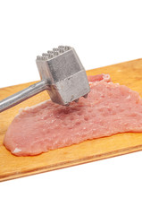 A piece of pork tenderloin on a wooden cutting board with a metal hammer for beating meat.