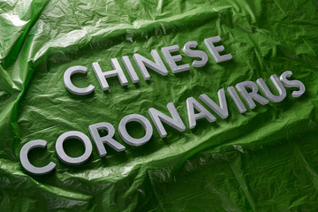 The words chinese coronavirus laid with silver metal letters on green crumpled plastic film -...