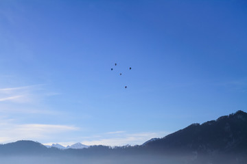 Fototapeta na wymiar Air Balloons flying in blue sky over misty lake Lucern, Swirtzerland
