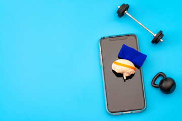 Brain training, neurology improvement app and mind workout concept with human brain with sweatband, barbell and free weights and smartphone isolated on blue background with copy space
