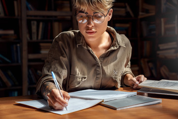 Young adult student girl writing in copybook, sitting in library