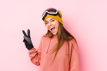 Young caucasian woman wearing a ski clothes isolated joyful and carefree showing a peace symbol with fingers.