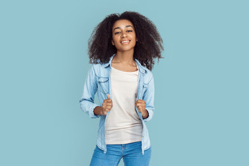 Freestyle. African girl standing isolated on gray holding jeans jacket smiling joyful