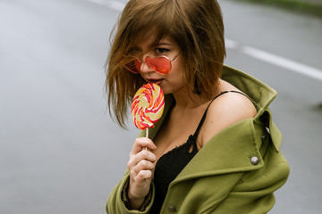 young european girl walks in rainy weather down the street with puddles of green cloak and eats...