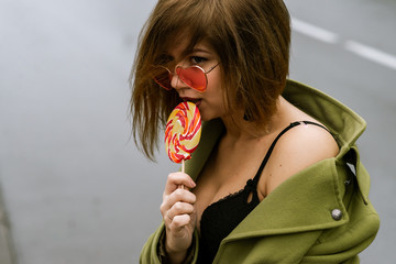 young european girl walks in rainy weather down the street with puddles of green cloak and eats...