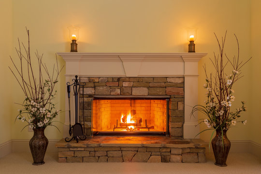 Cozy fire in a stone fireplace in a residential home with candles and flowers.