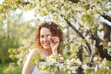 Young attractive girl walks in spring green park enjoying flowering nature. Healthy smiling girl spinning on the spring lawn. Allergy without