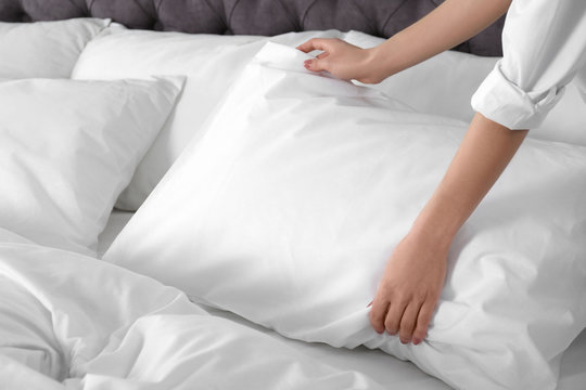 Woman fluffing soft pillow in bedroom, closeup
