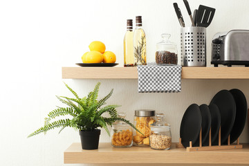 Wooden shelves with dishware and products on white wall. Kitchen interior idea