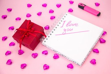 gift box with a red ribbon bow, on a pink background. Notepad for notes