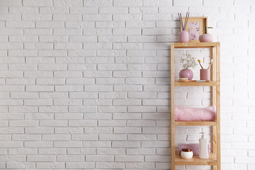 Shelving unit with toiletries near white brick wall indoors, space for text. Bathroom interior element
