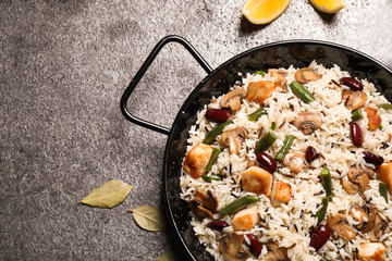 Delicious rice pilaf with chicken and vegetables on grey table, flat lay