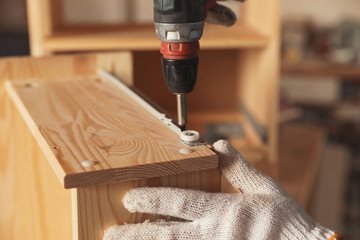 Professional carpenter twisting screw into wooden drawer in workshop, closeup