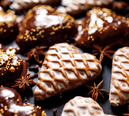 Gingerbreads in the shape of hearts covered with icing and chocolate on a black background, close up view. Traditional Christmas cookies