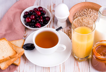 Delicious, healthy, hearty breakfast on the white table. Eggs, oatmeal, milk, tea, banana toast, homemade salted caramel, pancakes with fruit, orange juice. Top