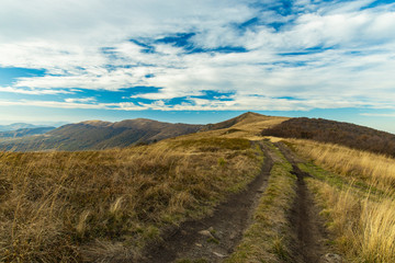 highland mountain ridge dirt trail route scenic landscape view horizon background cloudy blue sky