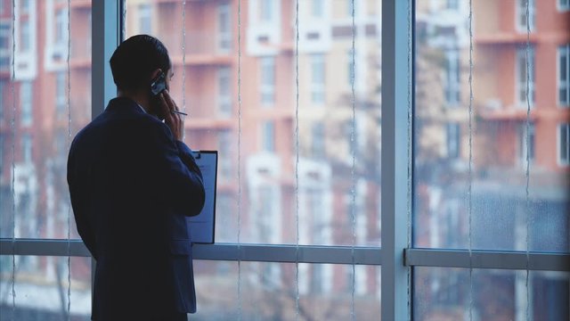 Businessman in formal suite stands in front of panoramic window with city view. Crop. Close up. Animation. 4K.