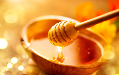 Honey dripping from honey dipper in wooden bowl.  Close-up. Healthy organic Thick honey dipping...