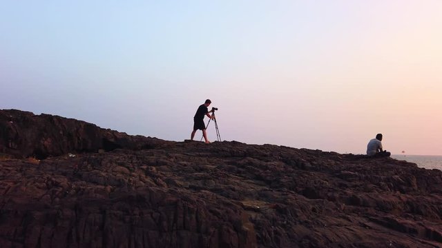 A man photographs a seascape during sunset on a cliff by the sea.